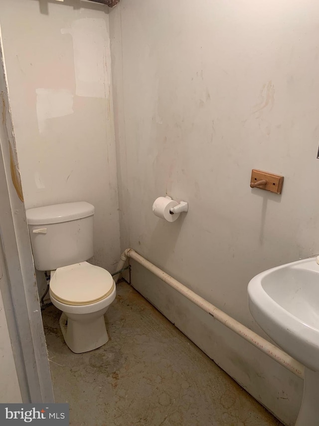 half bathroom featuring toilet, concrete floors, and a sink