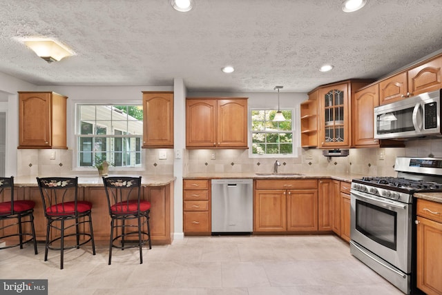 kitchen with stainless steel appliances, a sink, a kitchen breakfast bar, tasteful backsplash, and brown cabinetry