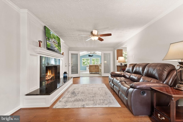 living area with a ceiling fan, a textured ceiling, a fireplace, wood finished floors, and crown molding
