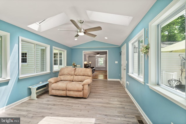 living area with a skylight, a ceiling fan, lofted ceiling, light wood-style floors, and plenty of natural light