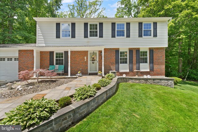 view of front of home with covered porch, an attached garage, a front yard, and brick siding