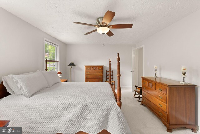 bedroom featuring light colored carpet, a textured ceiling, and a ceiling fan