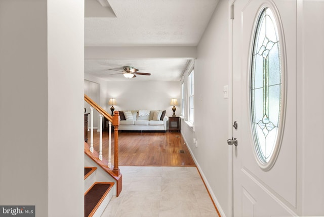 entryway featuring ceiling fan, stairway, a textured ceiling, and baseboards
