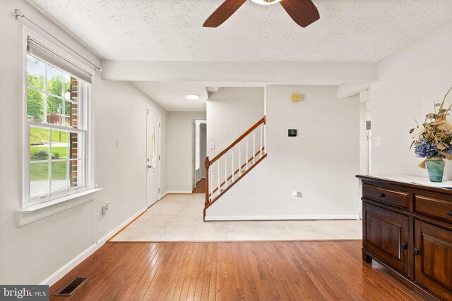 foyer with stairway, ceiling fan, a textured ceiling, baseboards, and light wood-style floors