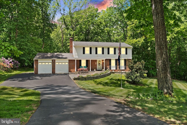 colonial inspired home featuring brick siding, driveway, an attached garage, and a chimney