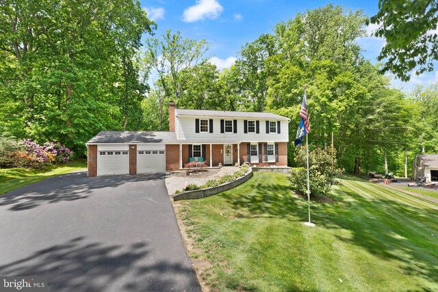 colonial inspired home featuring brick siding, asphalt driveway, a garage, covered porch, and a front lawn