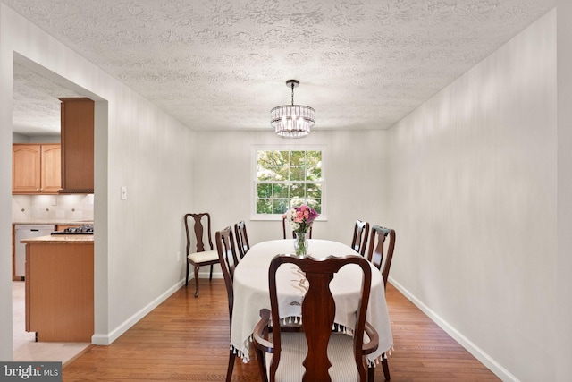 dining space featuring light wood-style floors, a textured ceiling, baseboards, and a chandelier