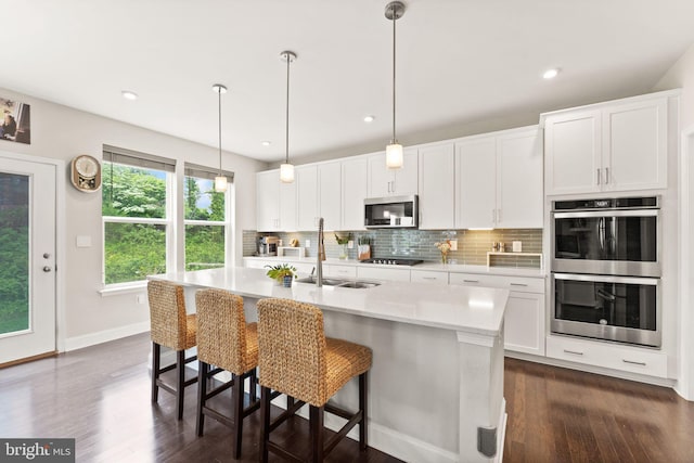 kitchen with stainless steel appliances, a sink, decorative backsplash, dark wood-style floors, and recessed lighting