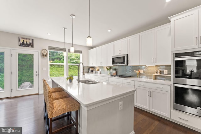 kitchen with a sink, stainless steel appliances, dark wood-style floors, tasteful backsplash, and an island with sink