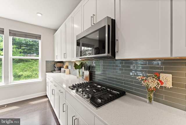 kitchen with appliances with stainless steel finishes, white cabinets, backsplash, and baseboards