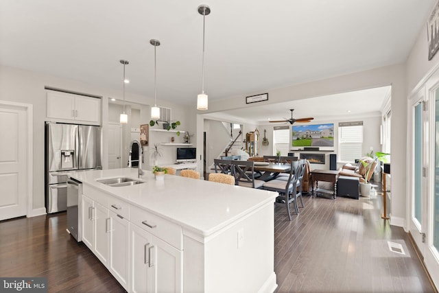 kitchen with a sink, appliances with stainless steel finishes, a lit fireplace, white cabinets, and dark wood-style flooring