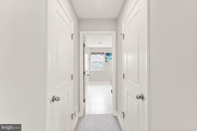 corridor featuring light colored carpet, baseboards, and light tile patterned floors