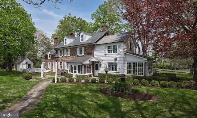 view of front facade featuring a chimney, a front lawn, an outdoor structure, a sunroom, and a shed