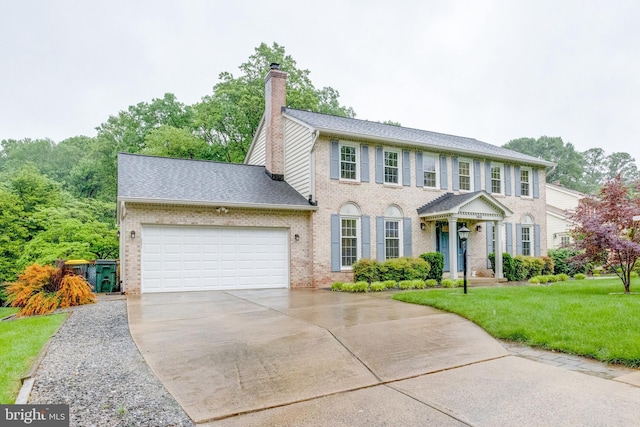 colonial-style house featuring brick siding, a garage, driveway, a front lawn, and a chimney