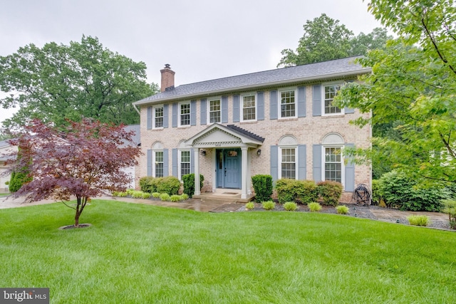 colonial house featuring a chimney, brick siding, and a front lawn