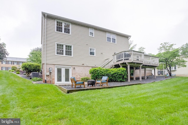 rear view of property with a deck, french doors, an outdoor fire pit, a lawn, and brick siding