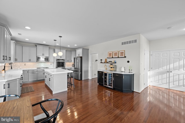 kitchen featuring appliances with stainless steel finishes, beverage cooler, a sink, a center island, and a breakfast bar