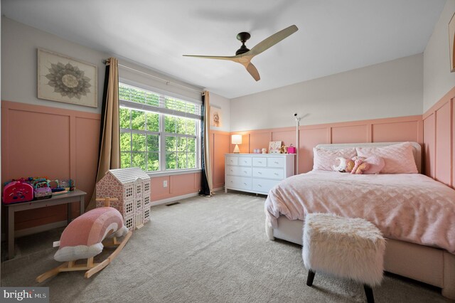 bedroom with a decorative wall, wainscoting, carpet floors, and ceiling fan