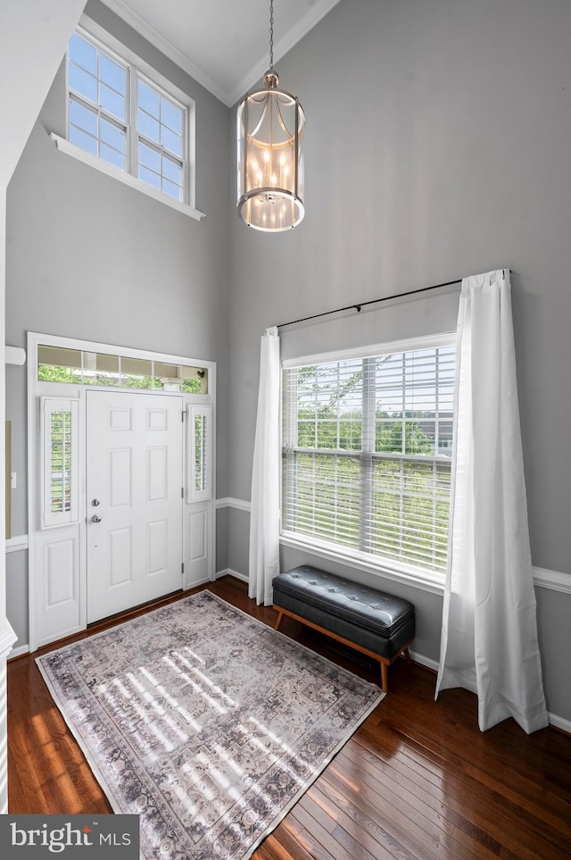 foyer entrance featuring a towering ceiling, crown molding, a chandelier, hardwood / wood-style flooring, and baseboards
