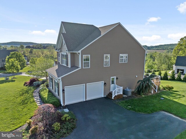 view of side of home featuring a garage, asphalt driveway, a yard, roof with shingles, and cooling unit