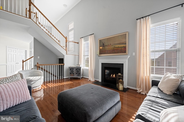 living room featuring plenty of natural light, wood finished floors, a high ceiling, and a fireplace with flush hearth
