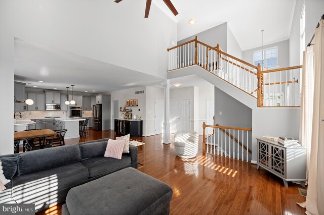 living room featuring a ceiling fan, dark wood-type flooring, a high ceiling, ornate columns, and baseboards