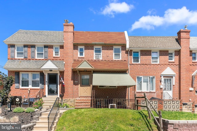 townhome / multi-family property featuring entry steps, a chimney, a front lawn, and brick siding
