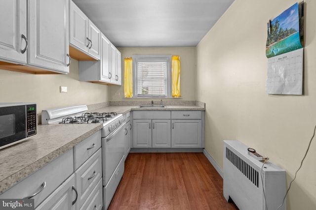 kitchen featuring white range with gas stovetop, stainless steel microwave, a sink, dark wood-type flooring, and light countertops