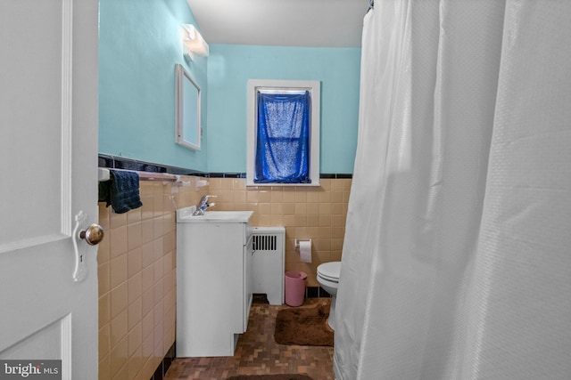 bathroom with tile walls, radiator heating unit, a wainscoted wall, toilet, and vanity