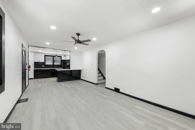 unfurnished living room with arched walkways, light wood-style floors, recessed lighting, a ceiling fan, and baseboards