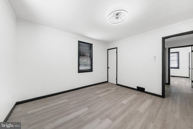 empty room with ornamental molding, light wood-style floors, and baseboards