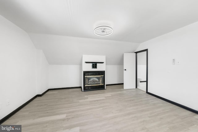 bonus room with lofted ceiling, light wood finished floors, a glass covered fireplace, and baseboards