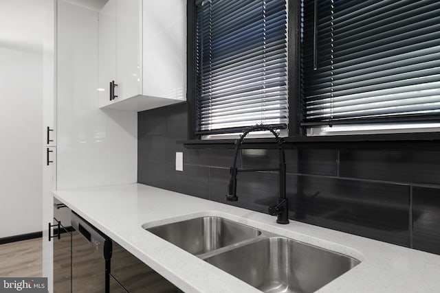 kitchen featuring backsplash, white cabinetry, light wood-style floors, a sink, and light stone countertops
