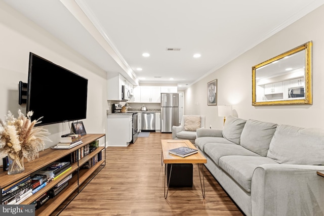 living area featuring crown molding, light wood-type flooring, and recessed lighting