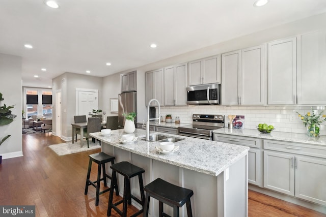 kitchen with appliances with stainless steel finishes, a sink, backsplash, a center island with sink, and recessed lighting