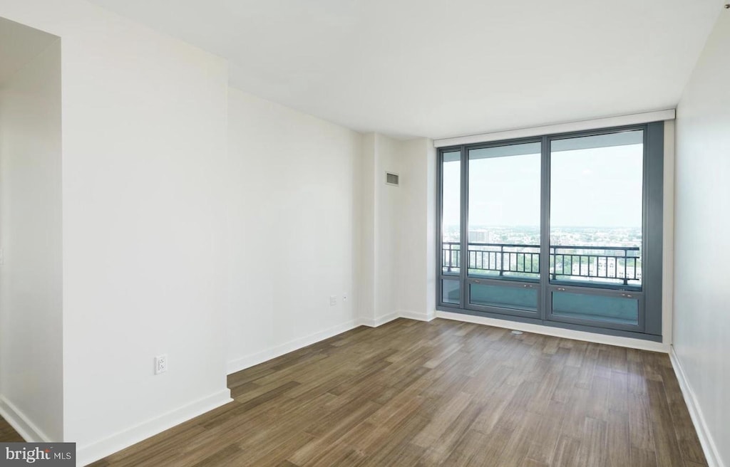 empty room with expansive windows, dark wood-style flooring, and baseboards