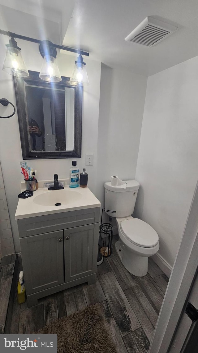 half bathroom with wood finished floors, vanity, and toilet