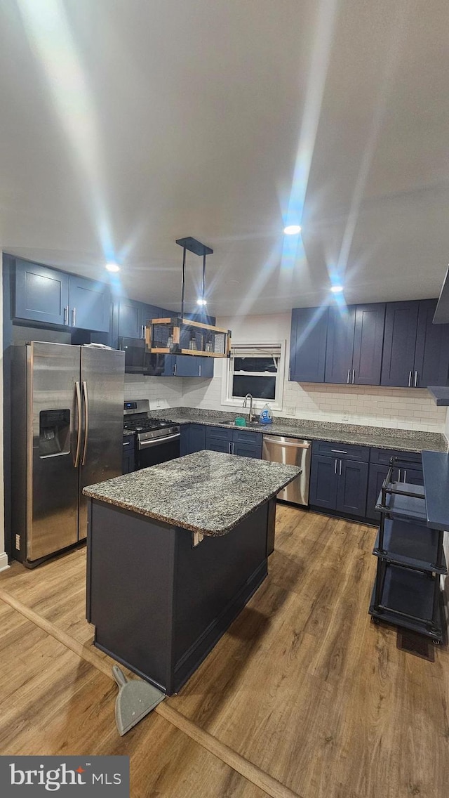 kitchen featuring appliances with stainless steel finishes, stone countertops, a kitchen island, a sink, and decorative backsplash