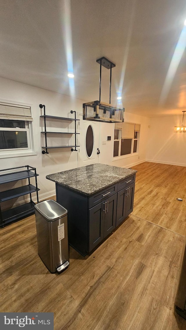 kitchen with wood finished floors, dark stone counters, a center island, baseboards, and dark cabinetry