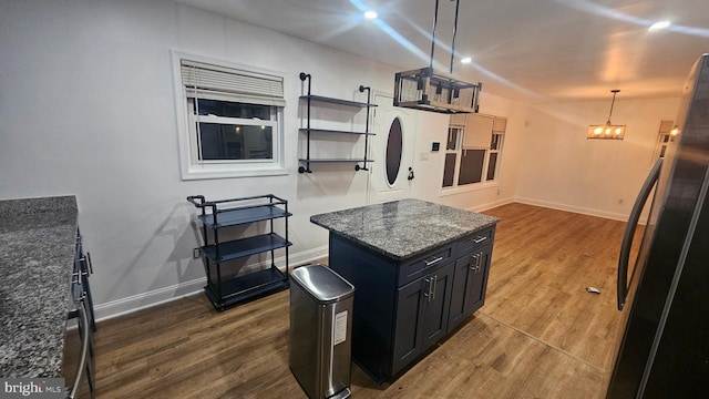 kitchen with freestanding refrigerator, baseboards, dark wood-style flooring, dark cabinetry, and dark stone counters