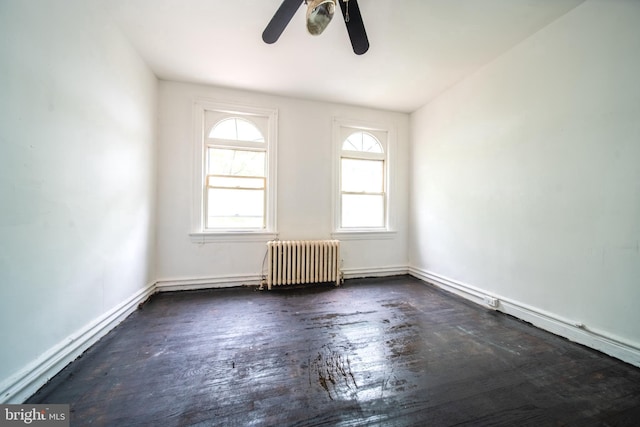 empty room with radiator, wood finished floors, a ceiling fan, and baseboards