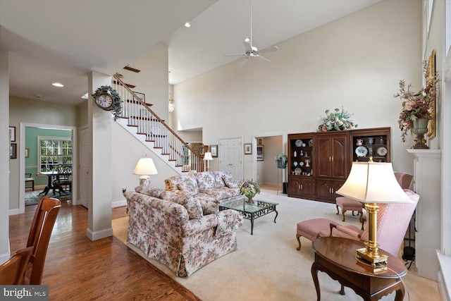 living room featuring stairs, ceiling fan, a towering ceiling, baseboards, and wood finished floors