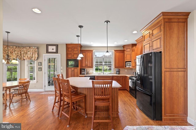 kitchen featuring black appliances, light countertops, brown cabinets, light wood-type flooring, and recessed lighting