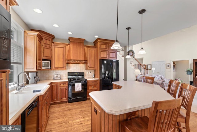 kitchen with black appliances, custom exhaust hood, a sink, light wood-type flooring, and a kitchen breakfast bar