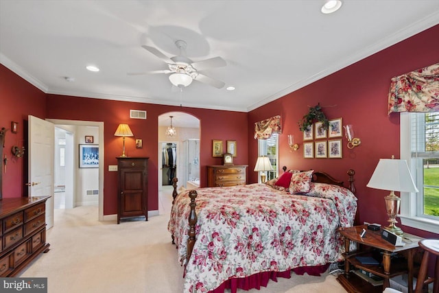 bedroom featuring light carpet, a walk in closet, recessed lighting, crown molding, and arched walkways