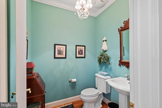 half bathroom featuring a chandelier, ornamental molding, toilet, baseboards, and a sink