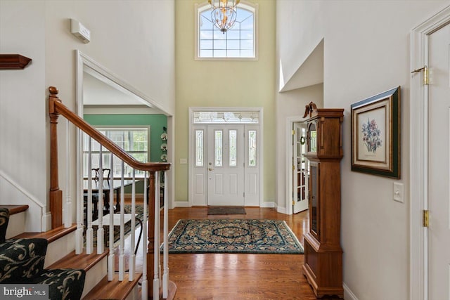 foyer featuring stairs, a high ceiling, wood finished floors, a chandelier, and baseboards