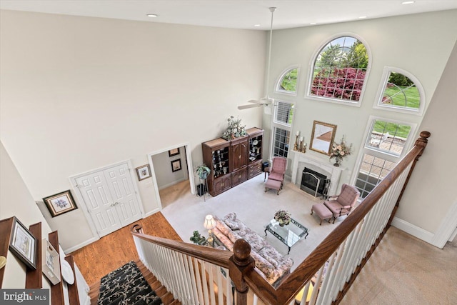 living room featuring a towering ceiling, healthy amount of natural light, baseboards, a fireplace with flush hearth, and ceiling fan