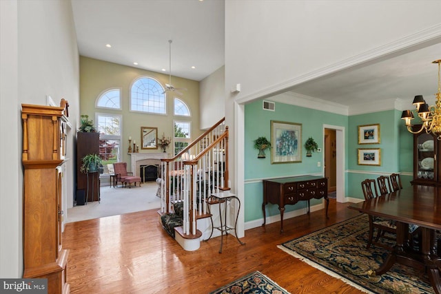 foyer entrance featuring a chandelier, a fireplace, wood finished floors, stairs, and a towering ceiling