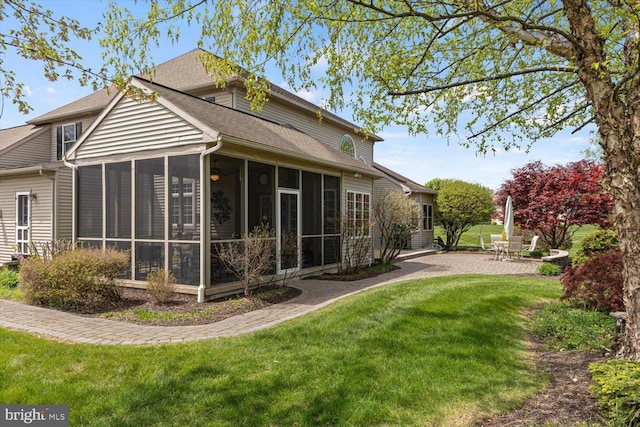 rear view of property featuring a shingled roof, a sunroom, a patio, and a lawn